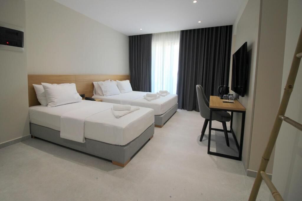 Une chambre d’hôtel avec deux lits, un bureau, une chaise, une télévision et une fenêtre avec des rideaux.