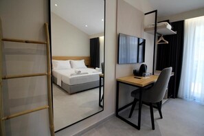 Quarto de hotel com cama, escrivaninha, cadeira, televisão e guarda-roupa.