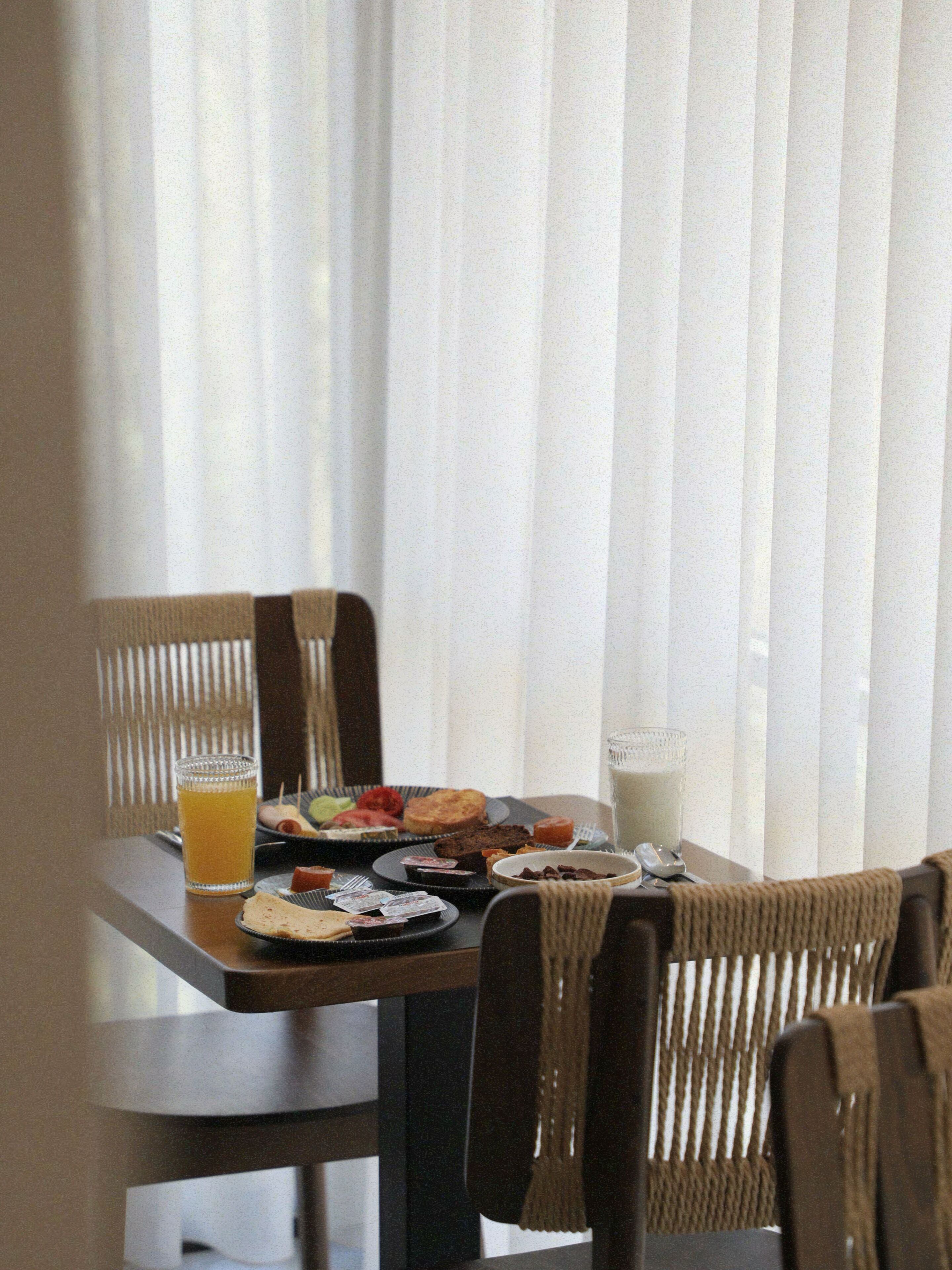 A dining table with plates of food, a glass of orange juice, and a glass of milk.