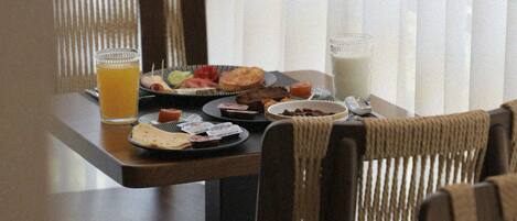 A dining table with plates of food, a glass of orange juice, and a glass of milk.