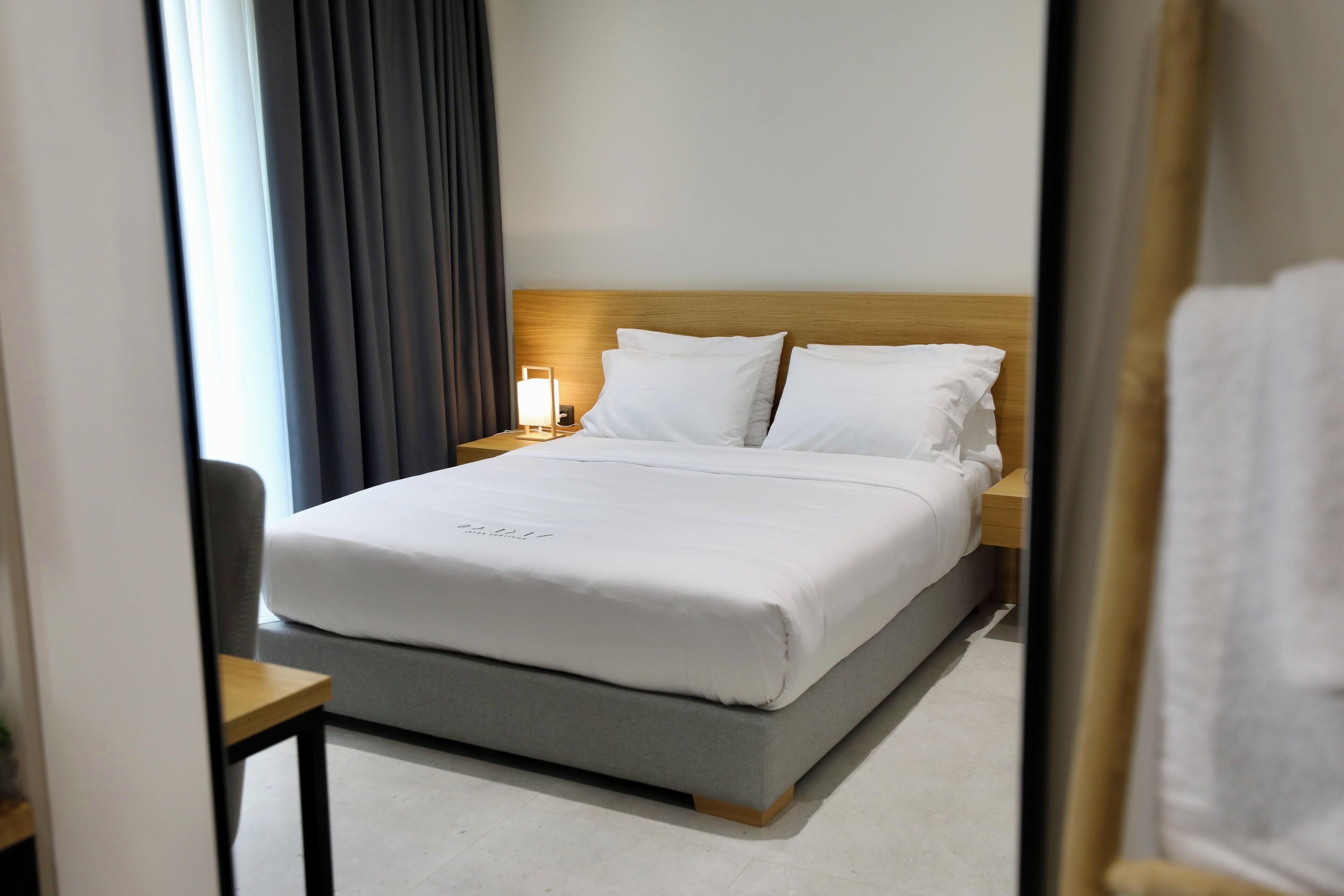 A hotel room with a bed, bedside table, lamp, and a chair.