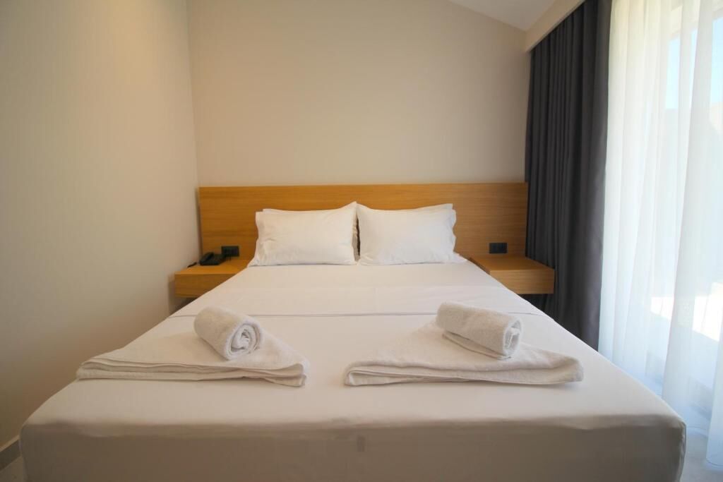 A hotel room with a large bed, two pillows, a wooden headboard, a nightstand, and two towels on the bed.