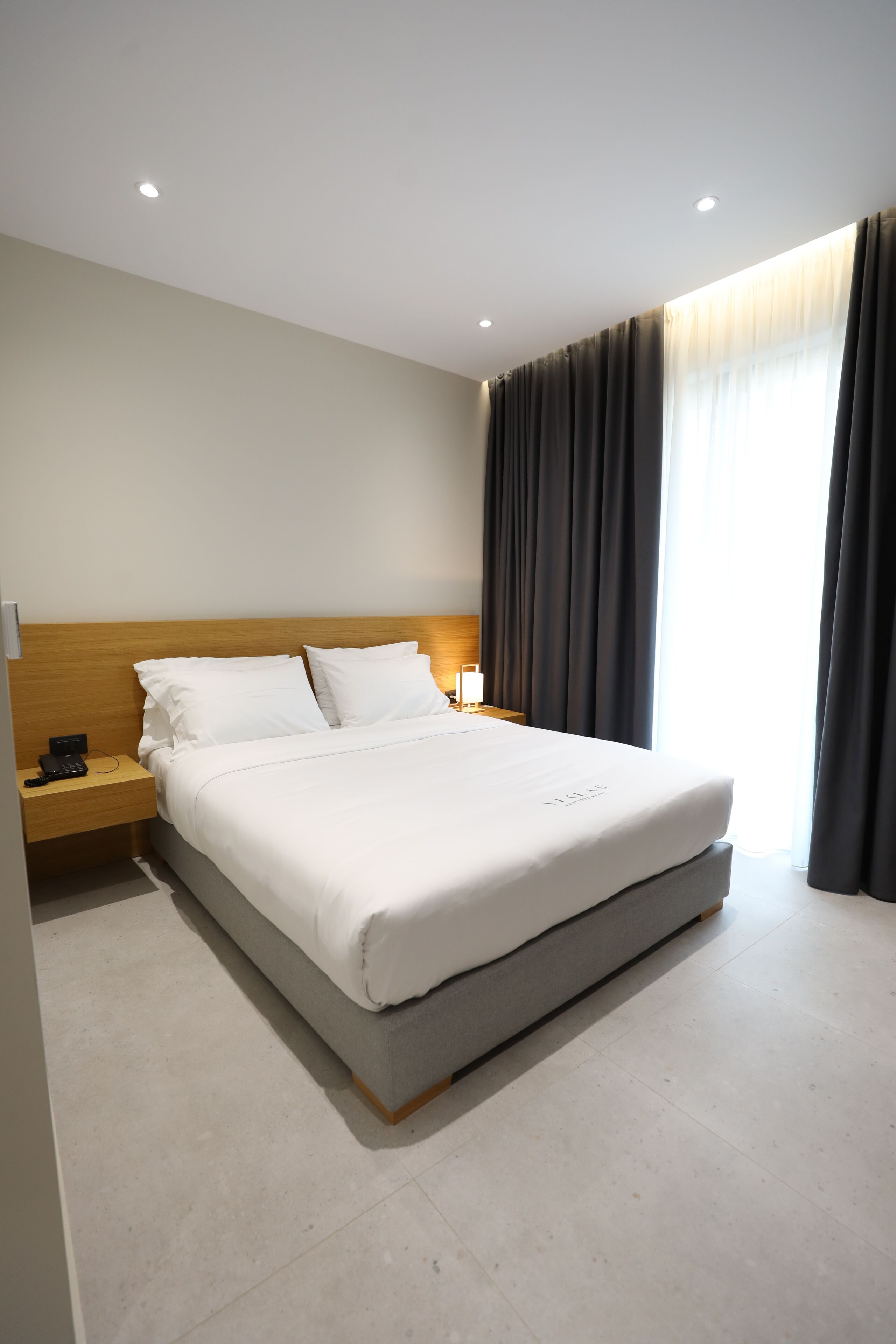 Una habitación de hotel con una cama grande, una mesita de noche y un ventanal con cortinas.