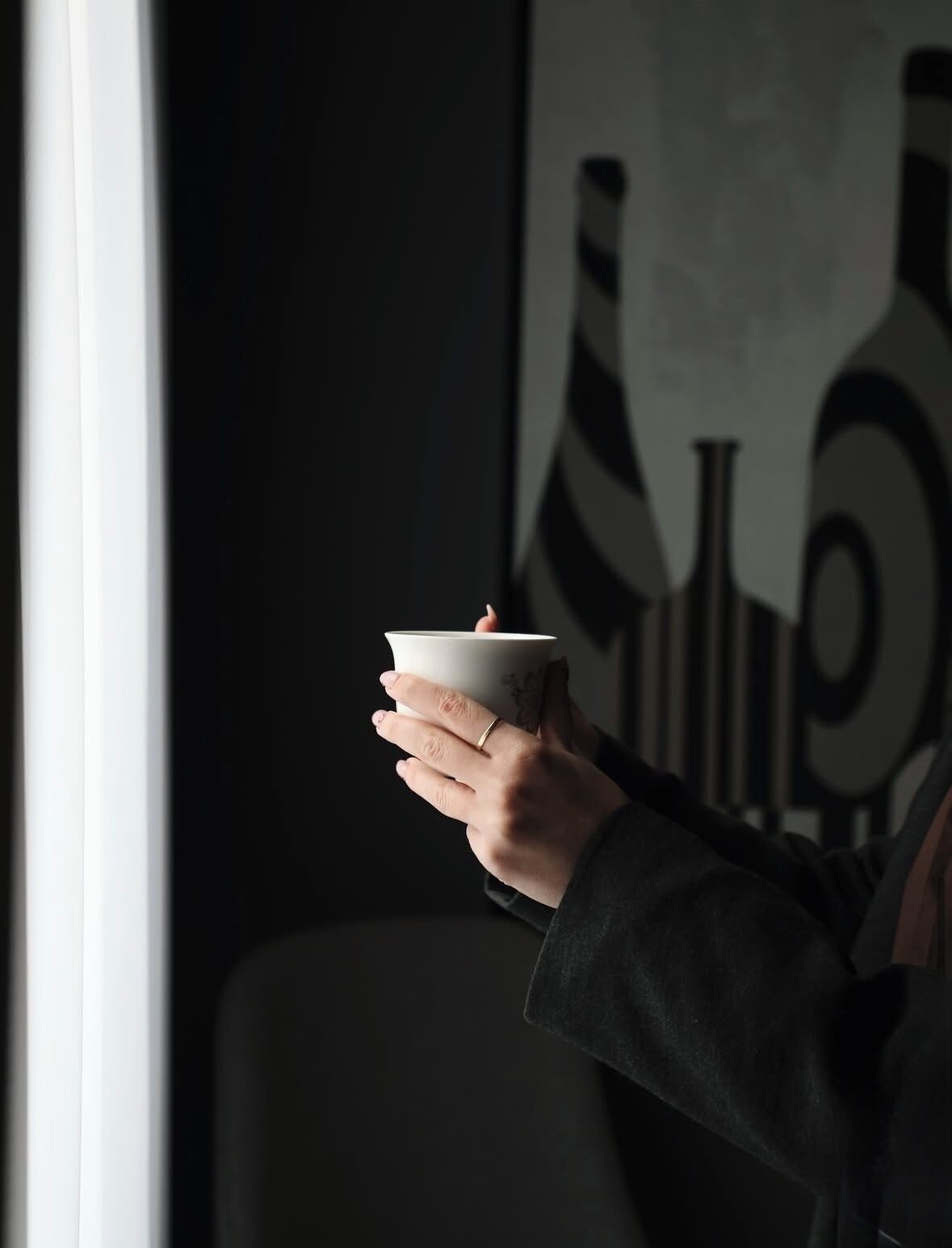 A person holding a white bowl with a spoon, in a room with a dark wall and a framed picture.