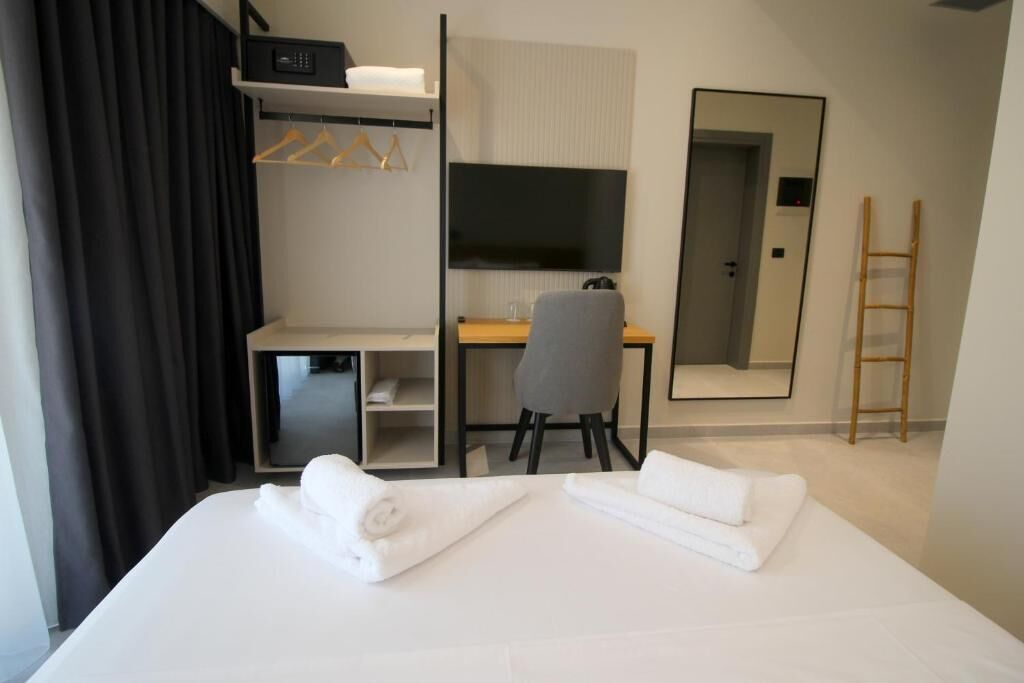 A hotel room with a bed, a desk, a chair, a TV, and a mirror.