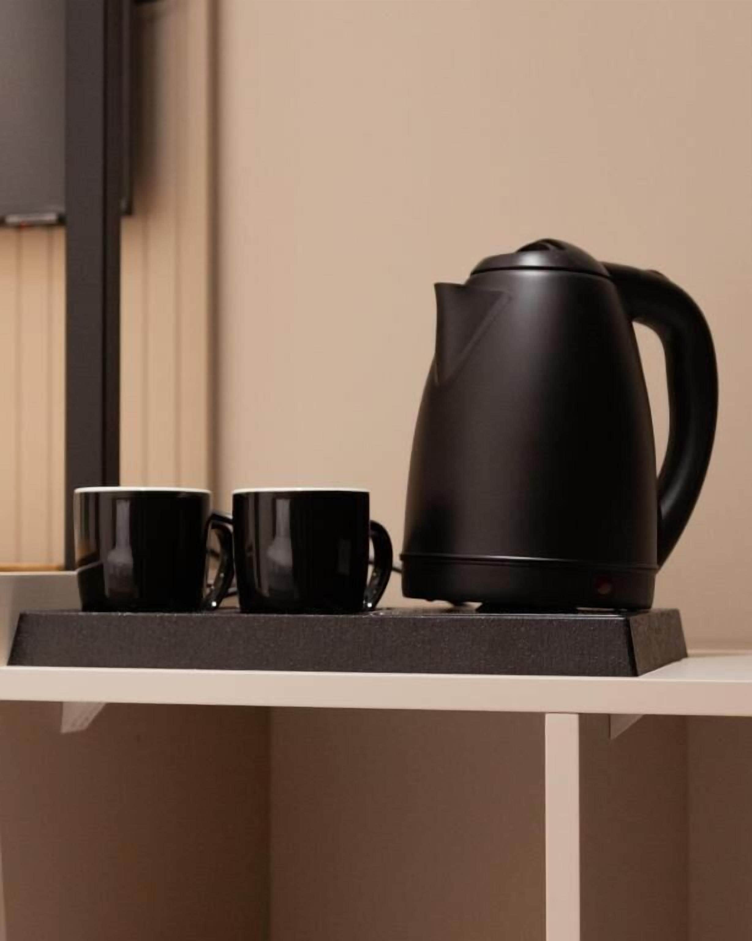 Una tetera eléctrica negra y dos tazas negras sobre un estante blanco.