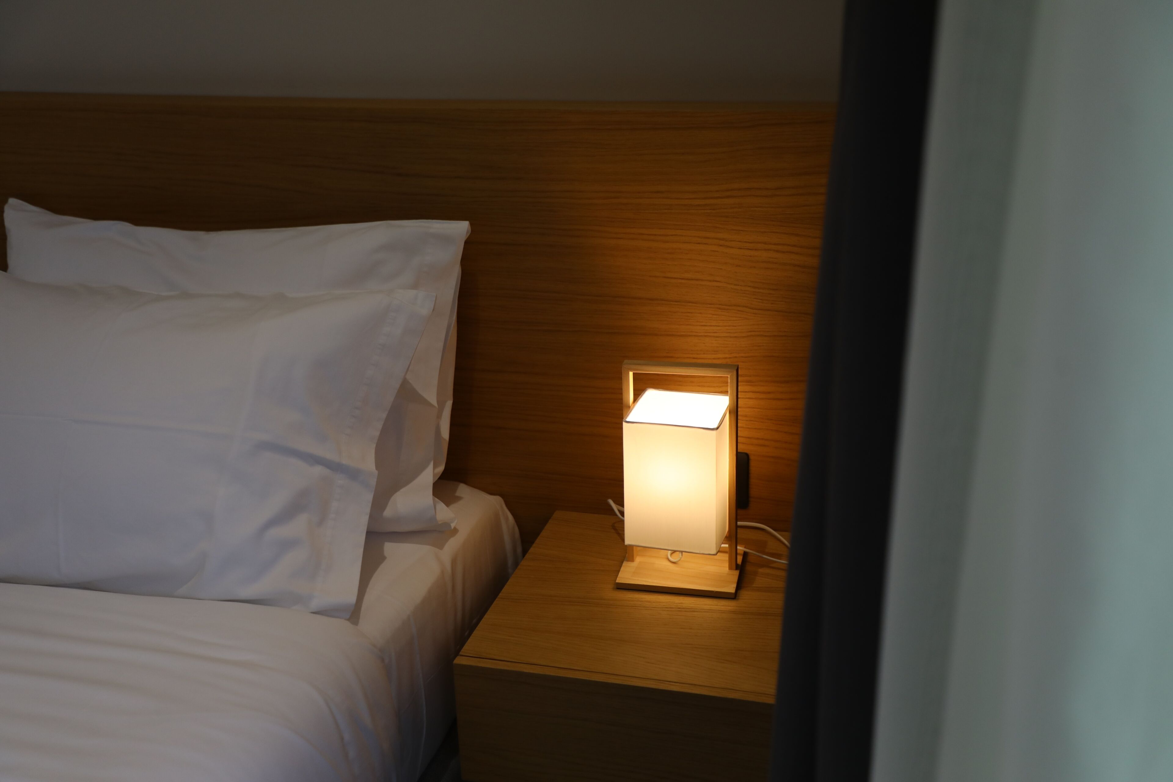 A neatly made bed with white linens, a wooden headboard, and a bedside table with a lit lamp.