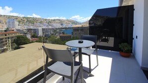 A balcony with a table and chairs, overlooking a cityscape with buildings and a body of water. - Niklas Boutique Hotel (Sarandë)