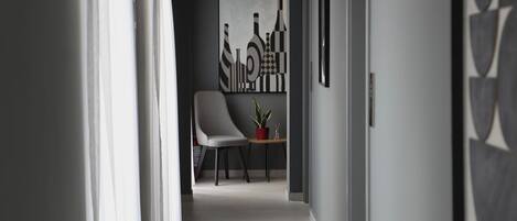 A hallway with a chair, a table with a plant, and artwork on the walls.