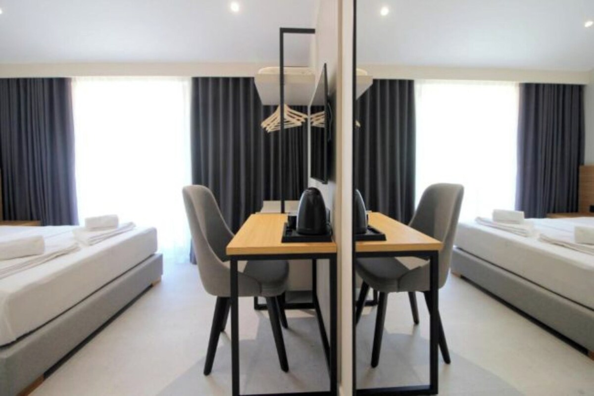 A hotel room with a bed, a desk with a chair, a small table, and a mirror.