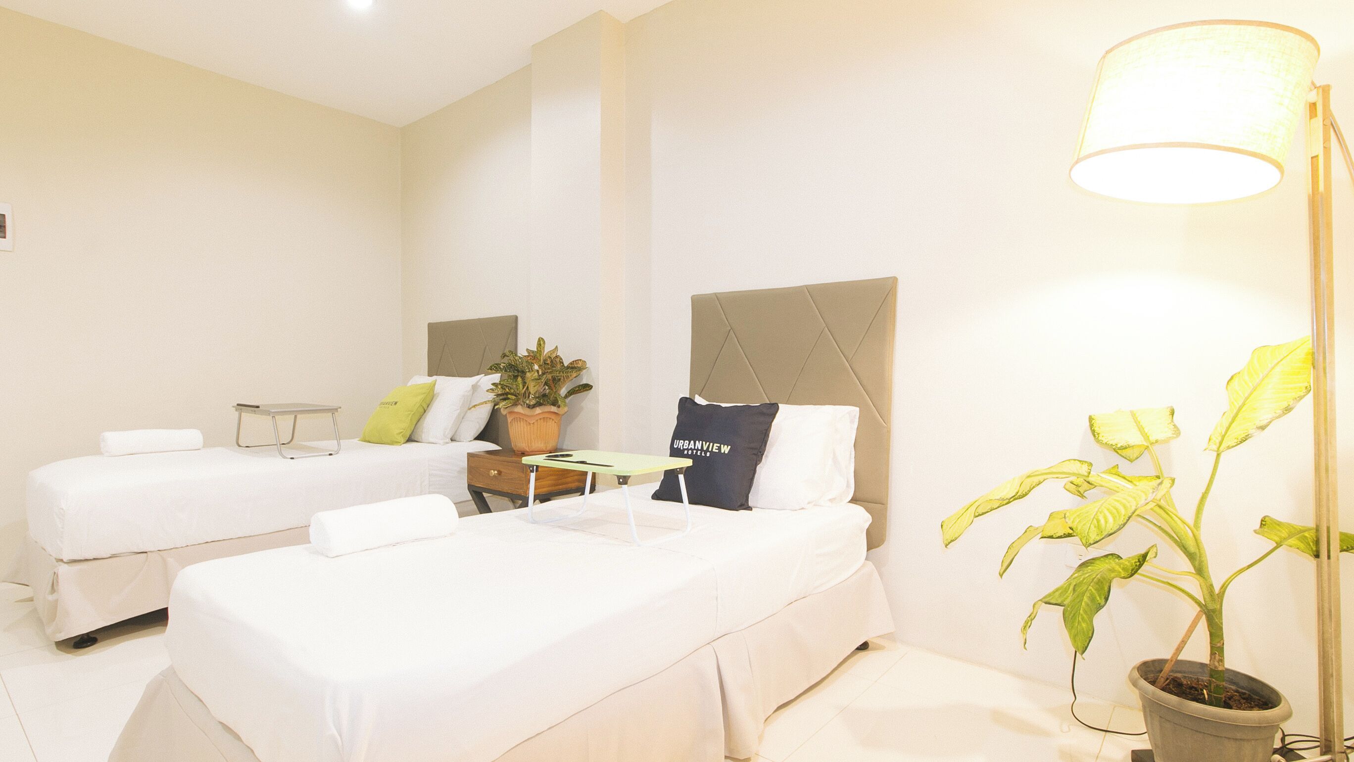Habitación de hotel con dos camas, una mesita de noche, una lámpara y una planta en maceta.