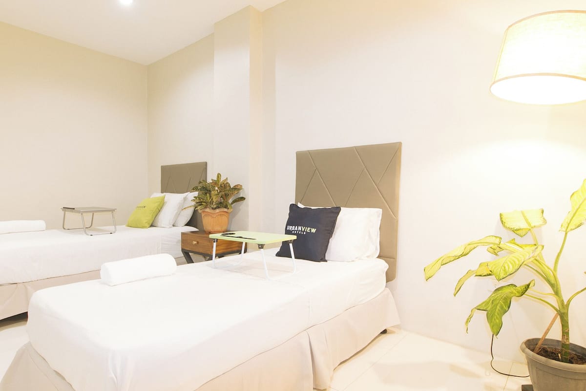 Une chambre d’hôtel avec deux lits, une table de chevet, une lampe et une plante en pot.