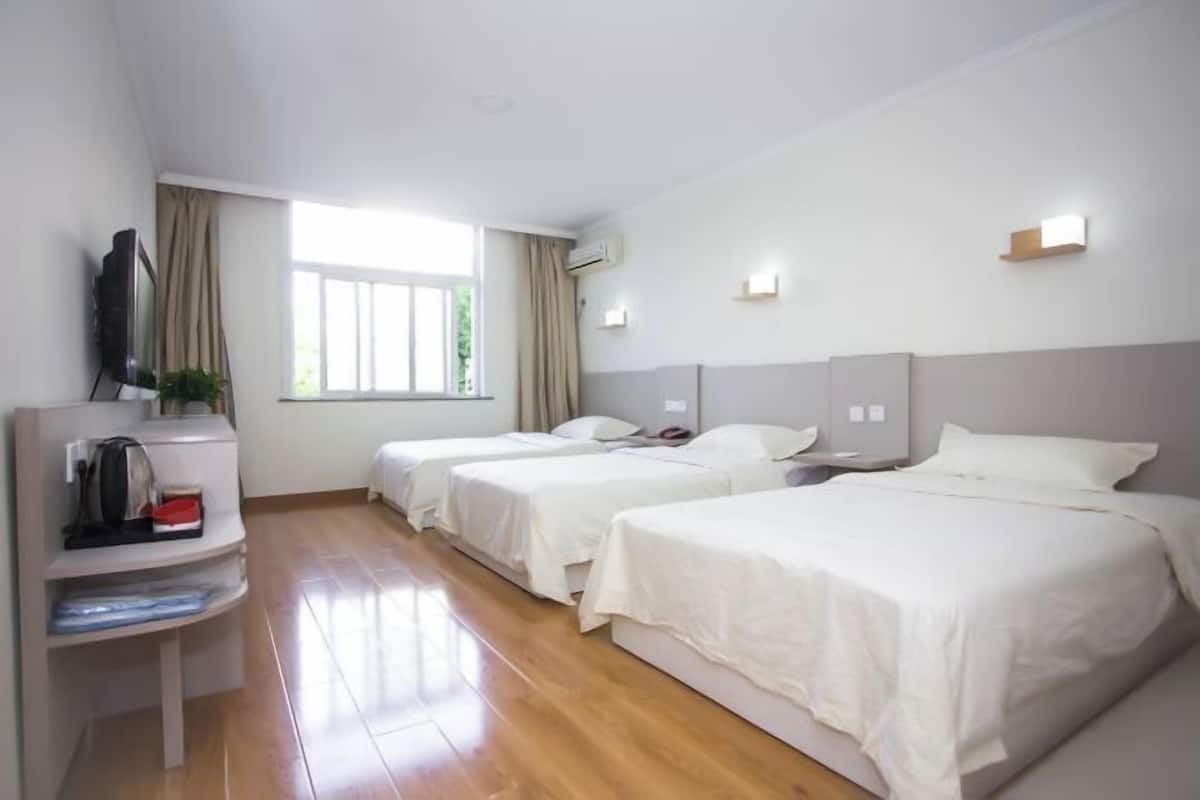 A hotel room with two beds, a TV, a desk with a kettle, and a window with curtains.