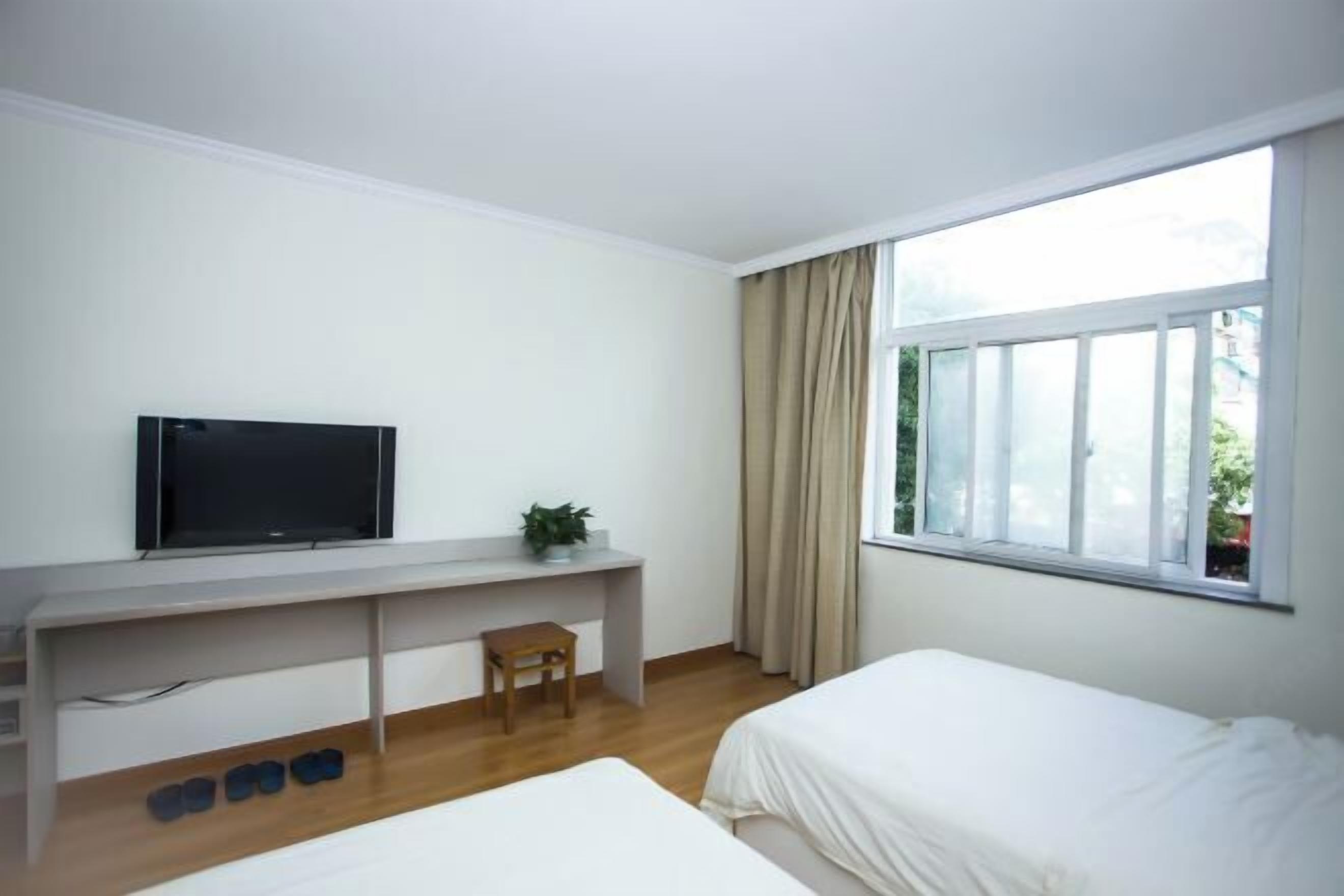 A room with a bed, a desk with a TV, a chair, and a window with curtains.