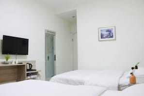 Habitación de hotel con dos camas, un televisor de pantalla plana montado en la pared, un escritorio con hervidor y un pequeño jarrón con flores secas.