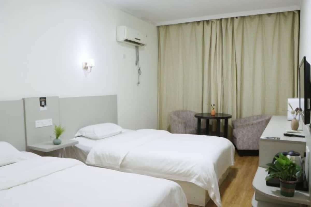 A hotel room with two beds, a desk, a chair, a TV, and a window with curtains.