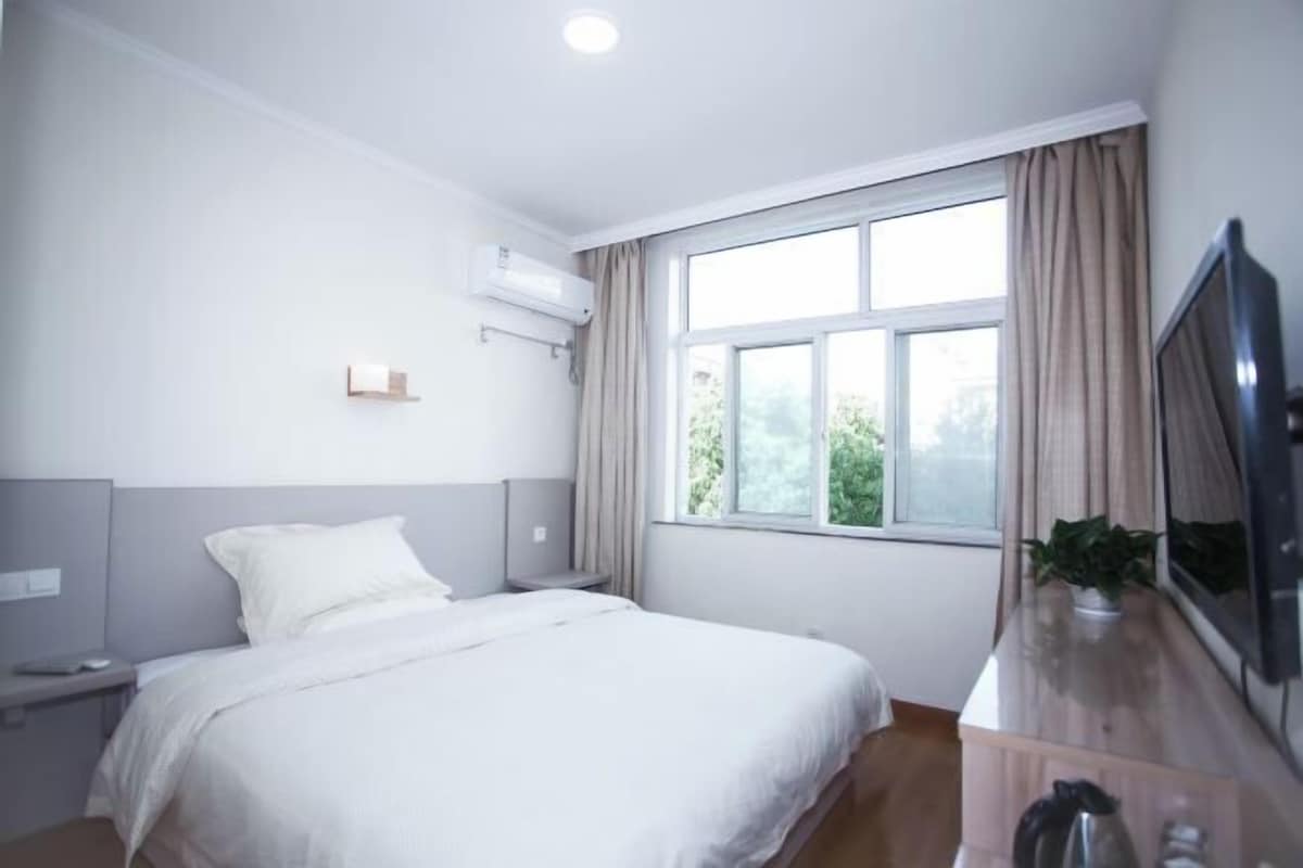 Habitación de hotel con cama, mesita de noche, televisor, ventana con cortinas y aire acondicionado.