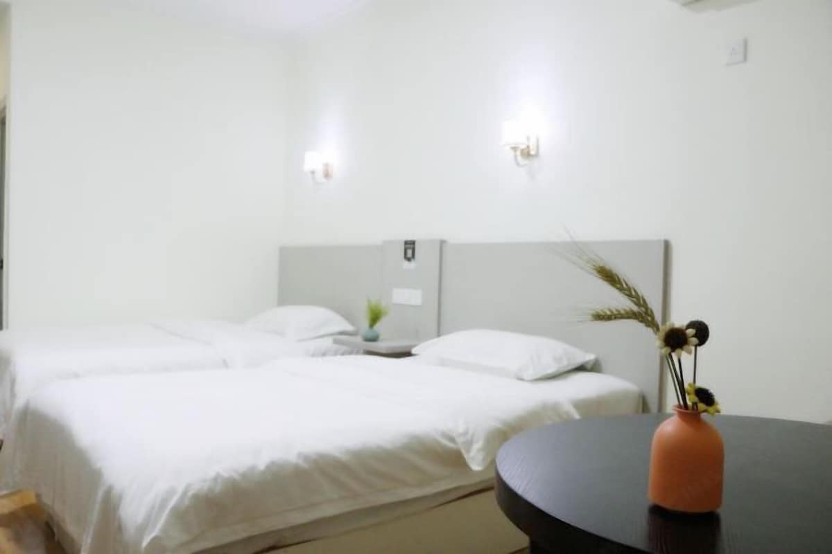 Una habitación de hotel con dos camas, una mesita con un florero y luces fijadas a la pared.