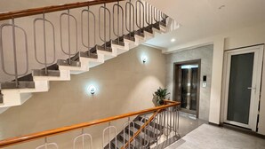 A modern interior with a wooden staircase, metal railings, and a marble floor. - Hotel Rudhav Palace (Ujjain)