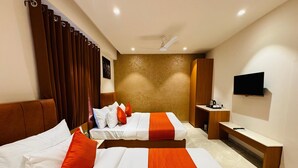 A hotel room with two beds, a TV, a desk, and a ceiling fan. - Hotel Rudhav Palace (Ujjain)