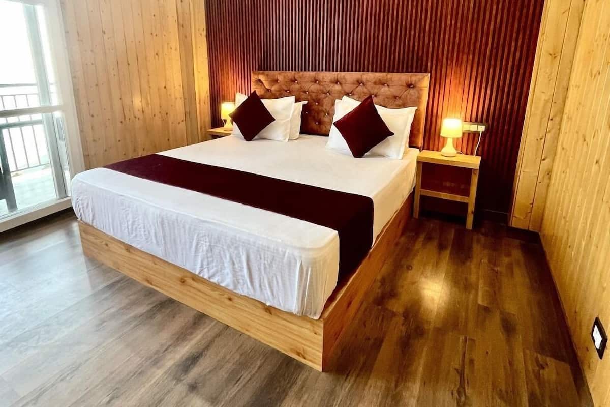 A large bed with a wooden frame and a tufted headboard, flanked by two bedside tables with lamps, in a room with wooden walls and floors.