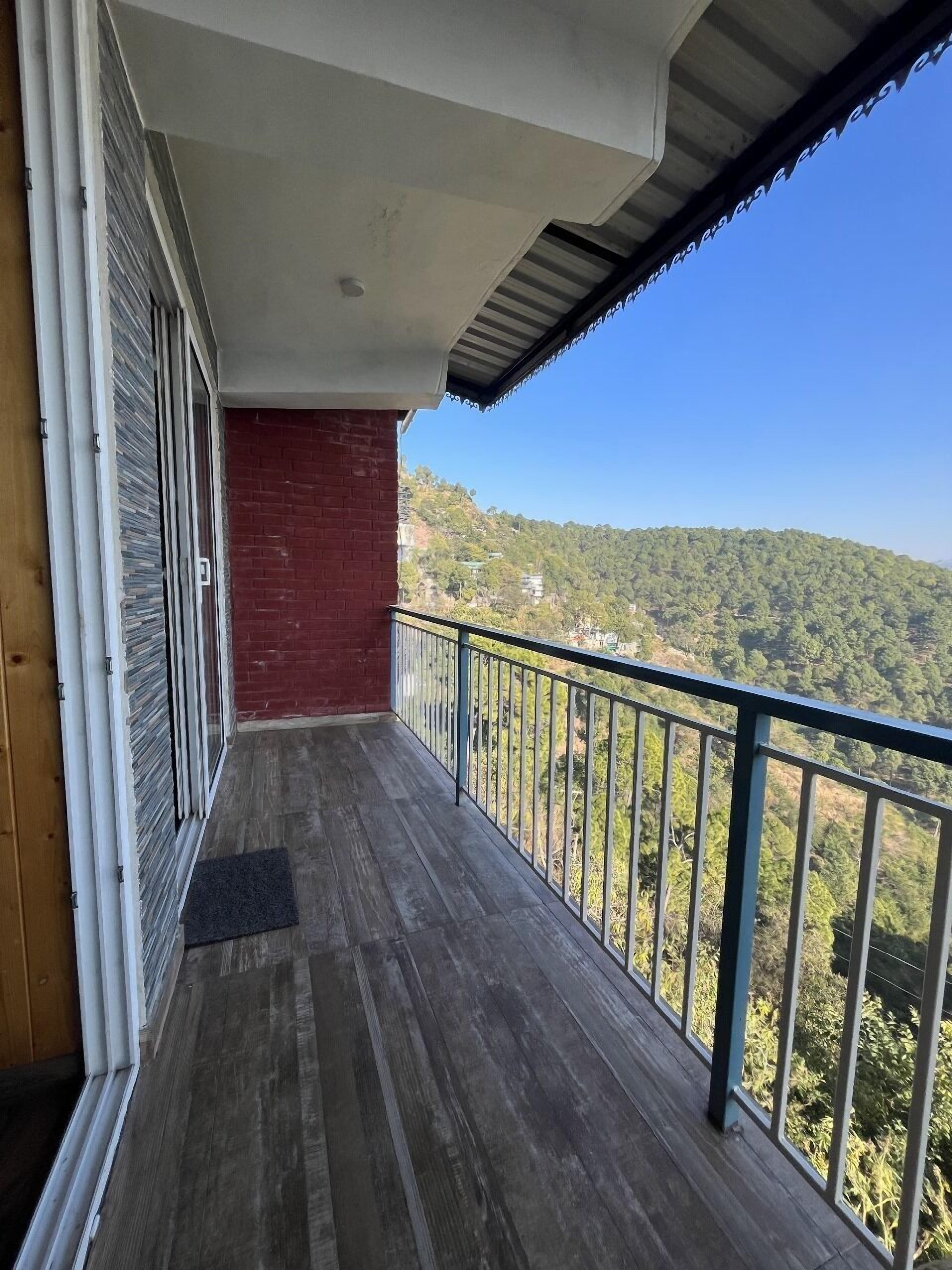 Un balcón con piso de madera, pared de ladrillo rojo y baranda de metal.