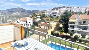 Una terraza en la azotea con piscina, edificios blancos y montañas al fondo.