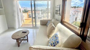 Una sala de estar con un sofá, una mesa de centro y vistas a través de un ventanal grande.
