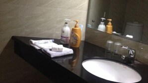 A bathroom with a black countertop, a white sink, and toiletries including a bottle of lotion and a bottle of shampoo. - Wenfeng Hostel (Huangshan City)