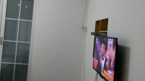 A room with a television mounted on the wall, a door with a window, and a small wooden shelf above the TV. - Wenfeng Hostel (Huangshan City)