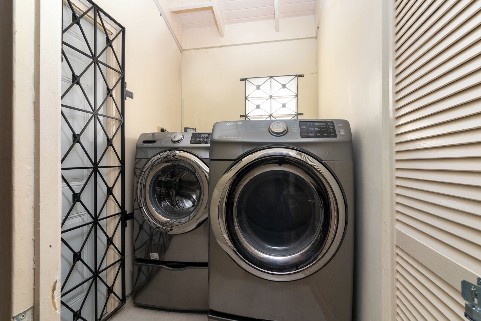 A compact laundry room with two front-loading washing machines and a metal gate.
