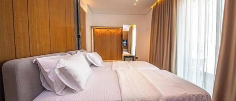 A hotel room with a large bed, wooden paneling on the walls, a wardrobe, and a view of the city through large windows.