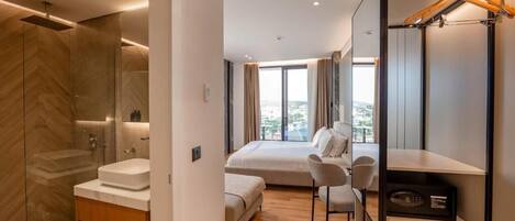 Una habitación de hotel moderna con una cama grande, un baño independiente con ducha, un área de estar y vistas a la ciudad.