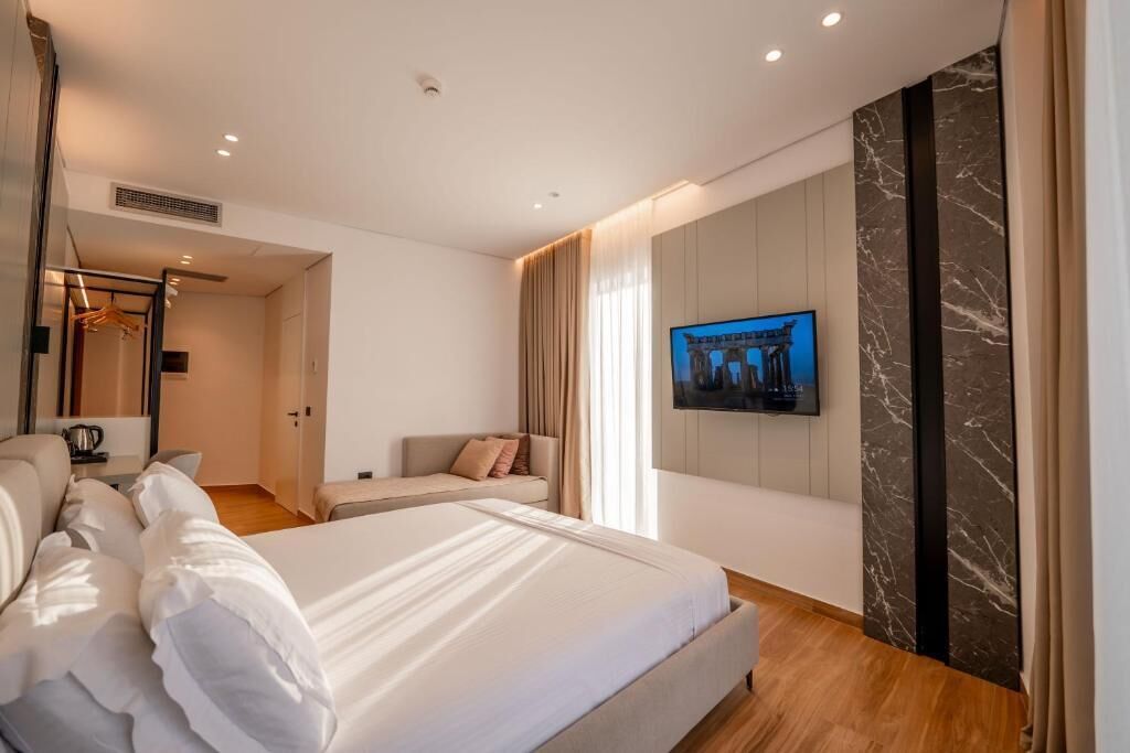 A modern hotel room with a large bed, a sofa, a television mounted on the wall, and a wardrobe.