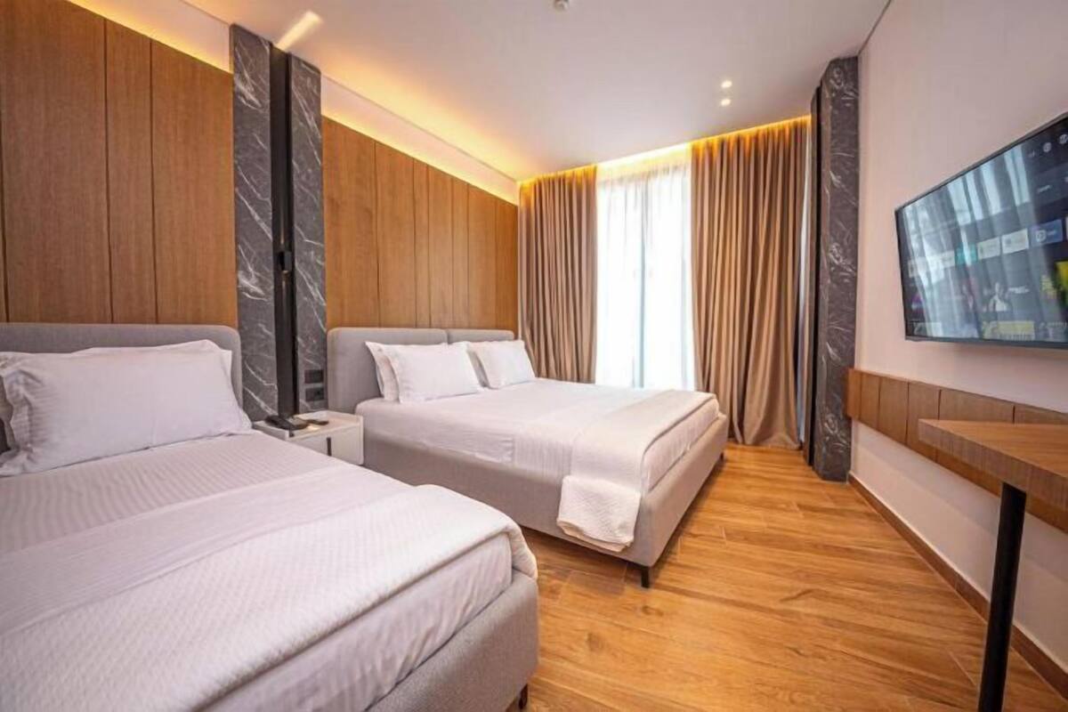 Habitación de hotel con dos camas, paneles de madera, televisor de pantalla plana y suelo de madera.