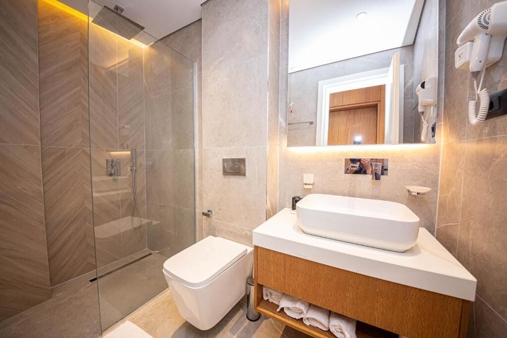 Un bagno moderno con doccia vetrata, un water bianco e un mobile lavabo con uno specchio grande e un asciugacapelli fissato alla parete.