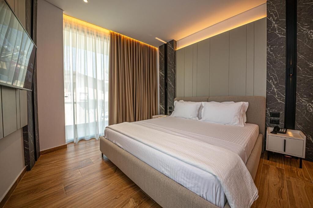 A modern bedroom with a large bed, a nightstand, a mirror, and a window with curtains.