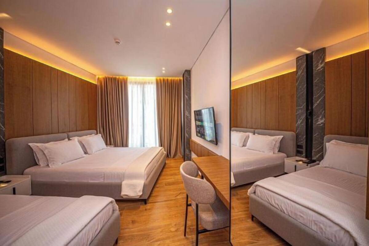 Habitación de hotel con dos camas, un escritorio y un espejo grande.