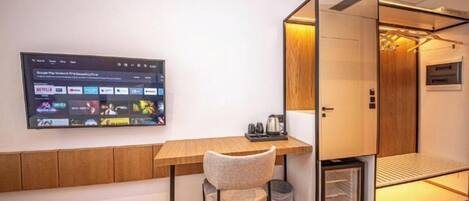 A modern room with a wooden desk, a chair, a TV displaying streaming services, and a compact storage unit.