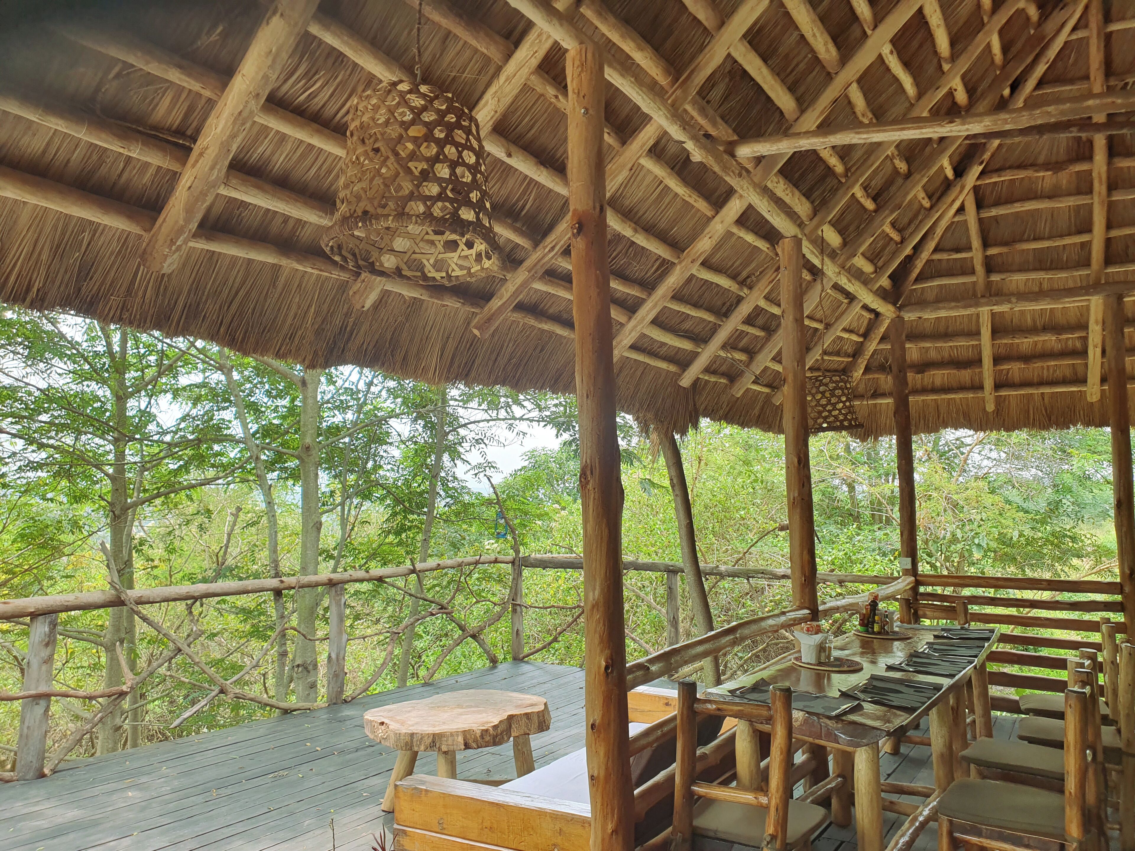 A wooden deck with a thatched roof, wooden railings, and a table with chairs.