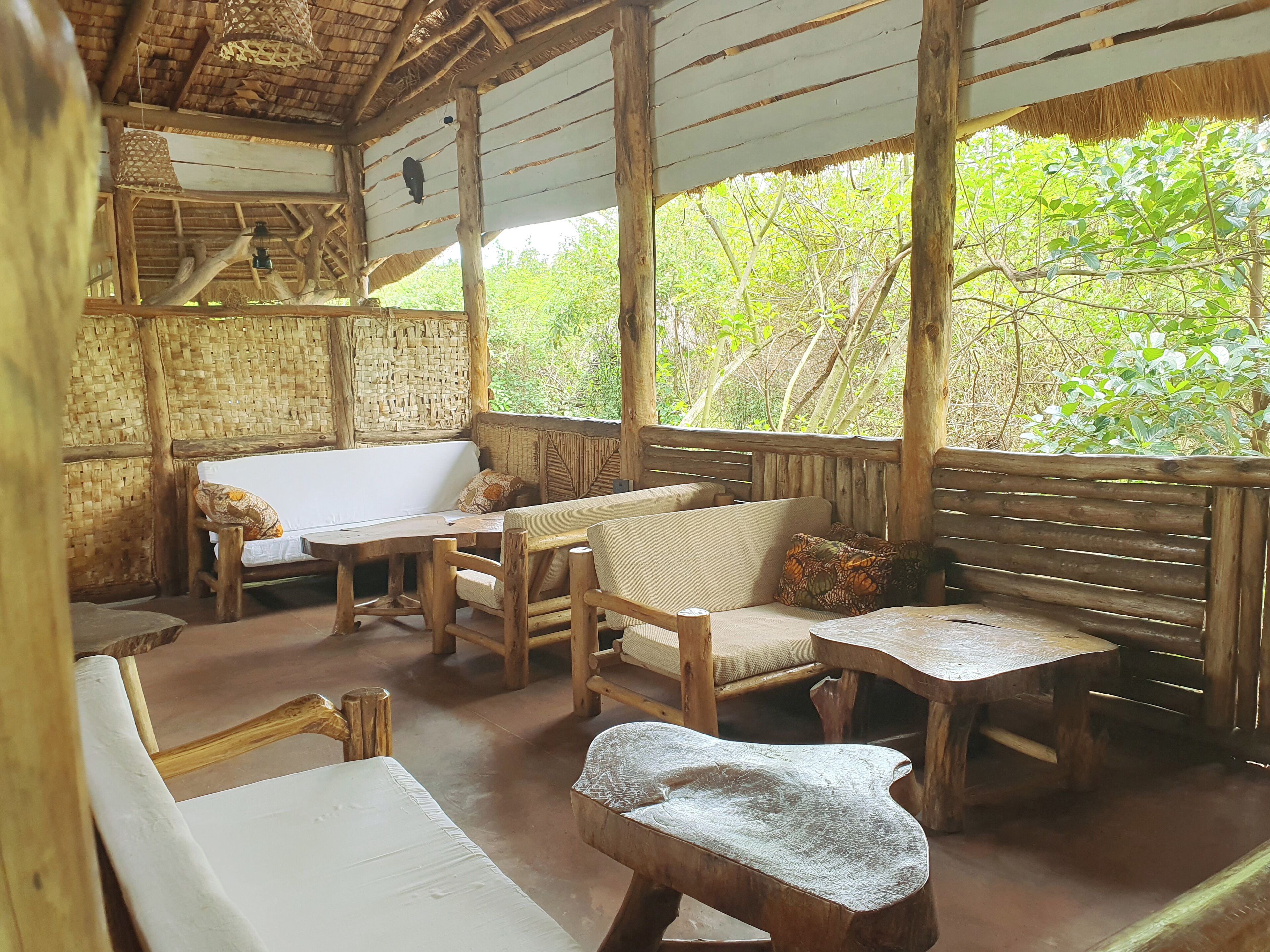 A rustic wooden room with a thatched roof, a woven wall, and a bench with cushions.