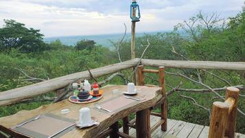 A wooden deck with a table set for a meal, overlooking a lush landscape.