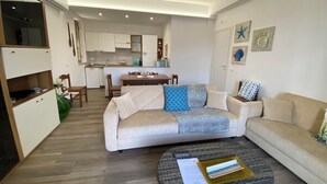 A modern living room with a sofa, coffee table, and a dining area in the background. - Villino Oleandro ad 1 Minuto a Piedi Dalla Spiaggia, Climatizzato e con Wifi (Santa Maria del Focallo)