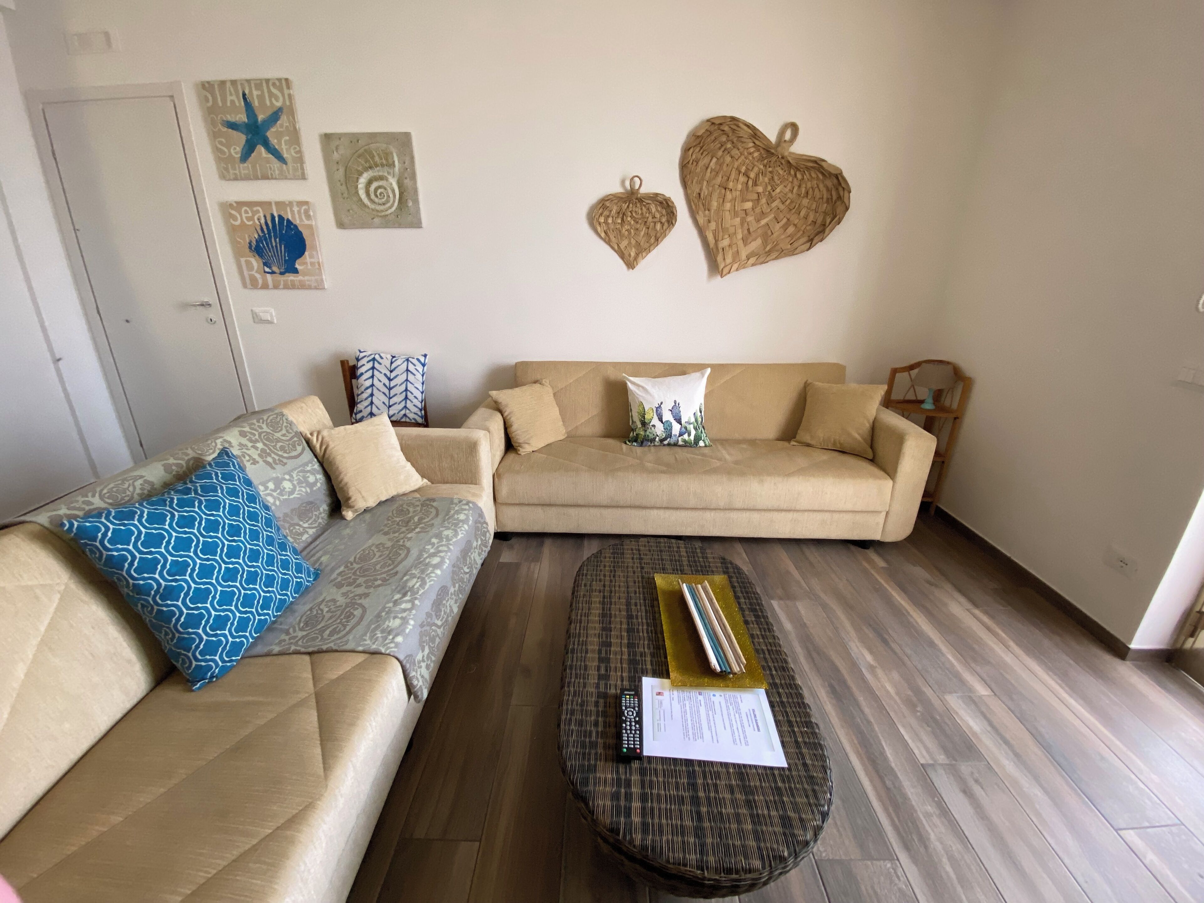 Ein Wohnzimmer mit zwei beigen Sofas, einem Couchtisch und Wanddekorationen, darunter Seesterne und herzförmige Objekte.