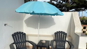 A small outdoor seating area with two black plastic chairs and a table, under a blue umbrella. - Villino Oleandro ad 1 Minuto a Piedi Dalla Spiaggia, Climatizzato e con Wifi (Santa Maria del Focallo)