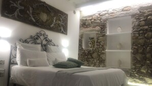 A bed with white bedding and decorative pillows, a stone wall, and a shelf with decorative items. - Beautiful private villa for 13 guests with private pool, A/C, TV and panoramic view (Capo D'orlando)