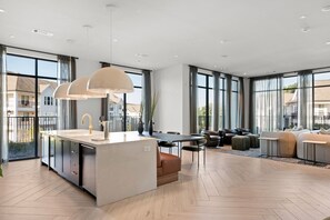 A modern kitchen with a central island, large windows, and a dining area with a sofa and table. - Upscale, New Apt | Pool | Long Stays (Athens)