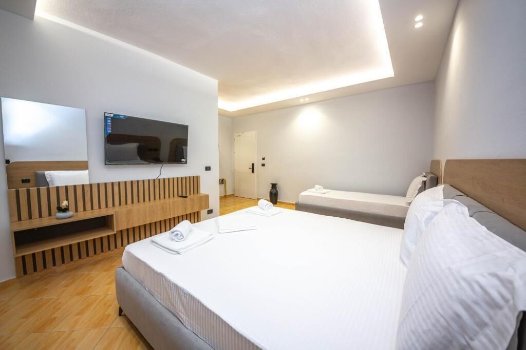 A modern hotel room with a large bed, a TV mounted on the wall, and a wooden console table.