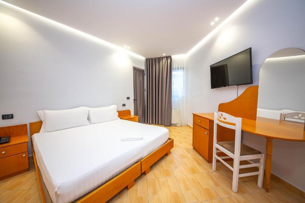 A modern hotel room with a large bed, a desk, a chair, a TV, and a window with curtains.