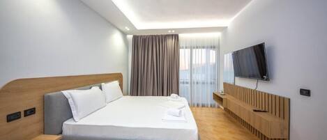A modern hotel room with a large bed, a TV mounted on the wall, and a wooden headboard.
